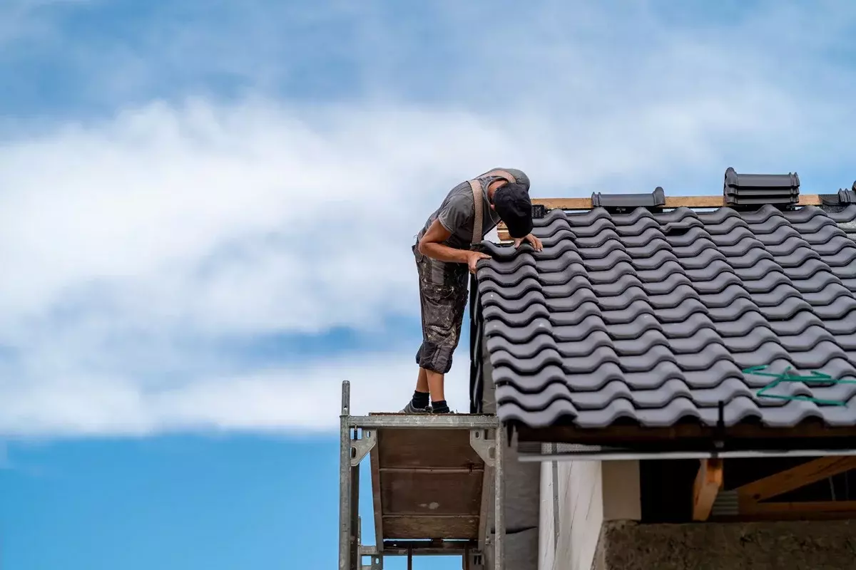 A professional local roofing technician sealing chimney flashing layers during a residential roof maintenance call
